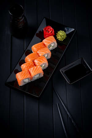 Philadelphia roll set with salmon, cucumber and cream cheese on a Japanese plate on a black wooden background with chopsticks and soy sauceの写真素材