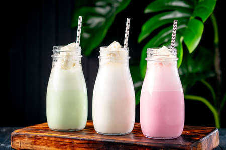 Set of different milkshakes with strawberries, mint and vanilla in glasses on a dark background with plantsの写真素材