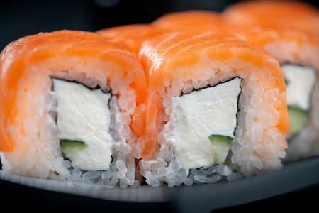 Philadelphia roll set with salmon, cucumber and cream cheese on a Japanese plate on a black wooden background, close upの写真素材