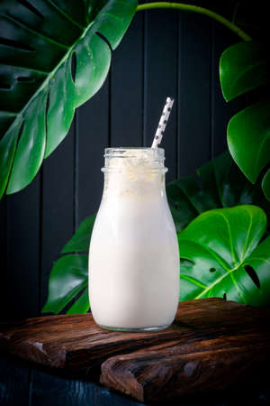 Classic Vanilla milkshake in a glass on a dark wooden background with banana leaves