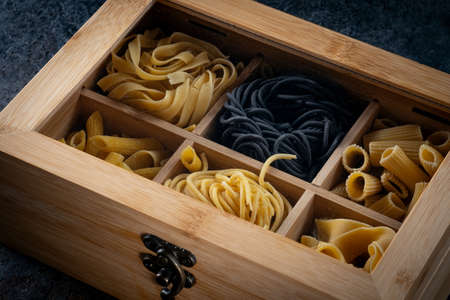 A wooden box with various types of dry pasta (spaghetti, rigatoni, tagliatelle, Penne, papardelle)...
