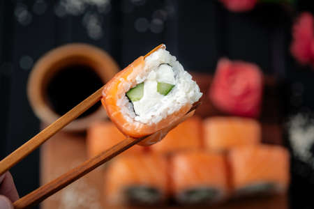 Philadelphia sushi roll in chopsticks on the background of a set of Japanese food, close-upの写真素材