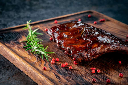 Grilled pork ribs with barbecue sauce on a wooden Board with spices and rosemary on stone backgroundの写真素材