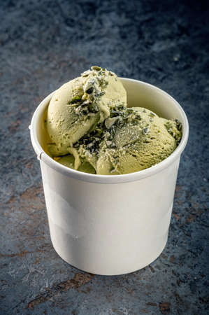 Pistachio ice cream balls with nuts in a paper white glass on a gray stone backgroundの写真素材