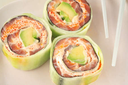 Fresh sushi roll with cucumber, salmon and avocado with chopsticks on plate. Healthy food Japanese cuisine. Close upの写真素材