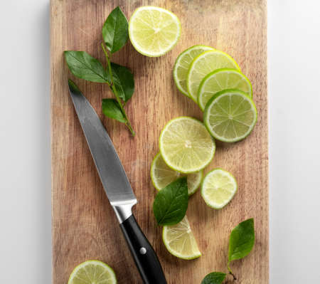 Fresh green lime sliced on pieces on a wooden Board with a knifeの写真素材