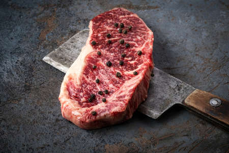 Juicy Raw new York beef steak and a butcher's hatchet close up on a dark backgroundの写真素材