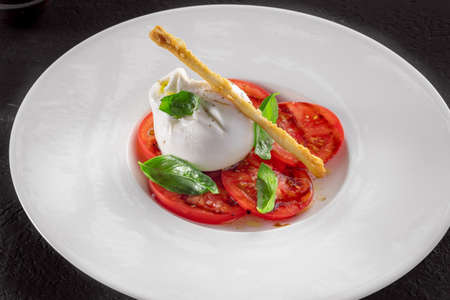 Burrata cheese and tomato salad with Basil and olive oil on a dark backgroundの写真素材