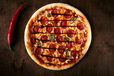 spicy pepperoni pizza with corn and jalapeno pepper on a dark wooden background. Top view of a cooked barbecue pizza. bannerの写真素材