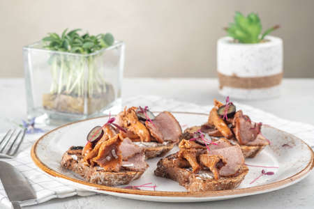 Open sandwiches on rye bread with pickled mushrooms chanterelles and ham on a white plate, close upの写真素材