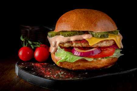 Big BBQ cheeseburger with beef, cheese, tomatoes, cucumbers on a black wooden boardの写真素材
