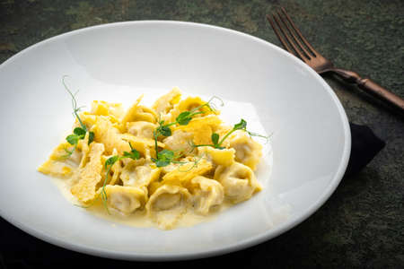 Tortellini with duck, croutons and cheese sauce on a white plate, close upの写真素材
