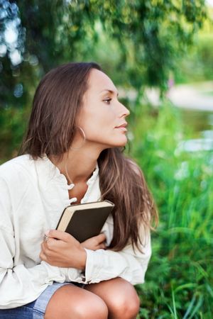 Thoughtful Young lady with book near the river in half face viewの写真素材