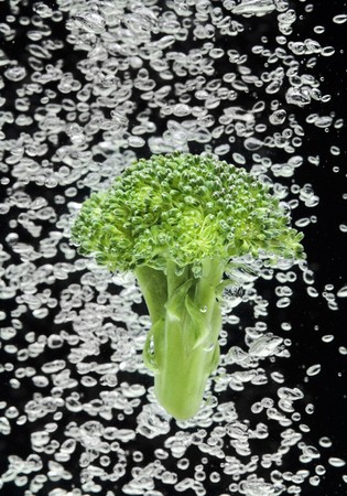 Green broccoli falling in water on black with air bubblesの写真素材