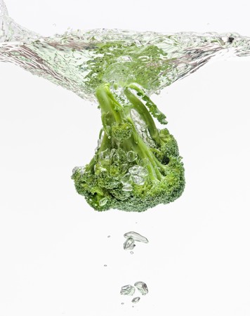 Green broccoli falling in water on white with air bubblesの写真素材