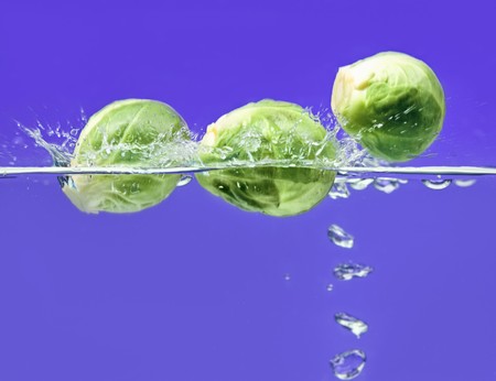 Three Brussels sprouts falling in water on blue with air bubblesの写真素材
