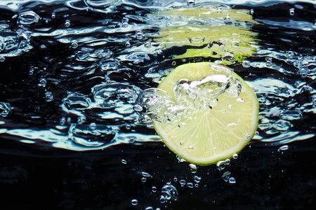 Slice of lime (lemon)  falling in water with air bubbles near surfaceの写真素材