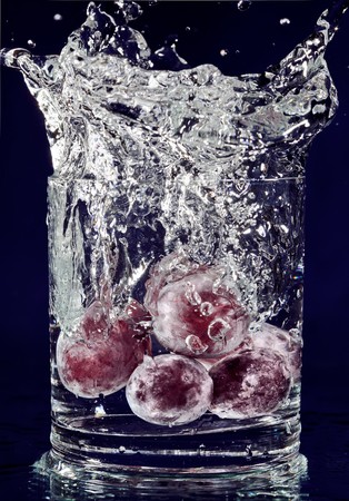 Bunch of red grapes falling down in glass with water on deep blueの写真素材