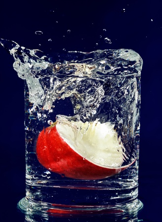 Slice of red apple falling down in glass with water on deep blueの写真素材