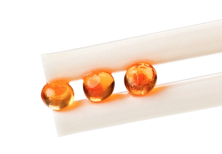 Three red salmon caviar ball in chopsticks, isolated on white macro