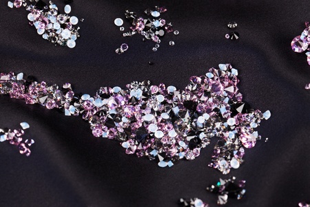 Diamond (small purple jewel) stones heap over black silk cloth backgroundの写真素材