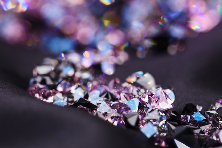 Diamond (small purple jewel) stones heap over black silk cloth backgroundの写真素材