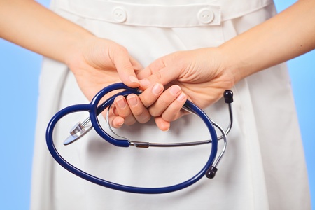 Doctor holding stethoscope behind her back, waist-high portrait on blueの写真素材