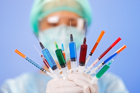 Young woman doctor with many multicolor syringes in hands on blueの写真素材