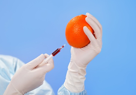 Doctor's hands injecting orange fruit with syringe on blueの写真素材