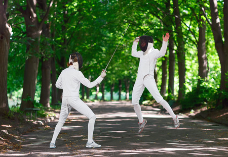 Two rapier fencer women fighting over park alley, attacking each other in jumping
