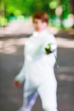 Tip of rapier held by fencer woman staying in park alley, shallow depth of field