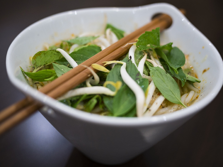 Beautiful and appetizing photo of a traditional vietnamese chicken noodle soup, also know as Pho Ga. In a white bowl with wooden background and luxurious wooden chopsticks. Amazing green mint and basil.の写真素材