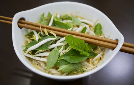 Beautiful and appetizing photo of a traditional vietnamese chicken noodle soup, also know as Pho Ga. In a white bowl with wooden background and luxurious wooden chopsticks. Amazing green mint and basil.の写真素材