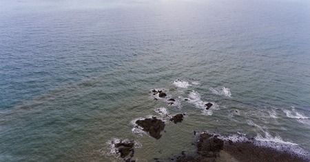 Amazing rocky beach shore. Picture of brown and black rocks surrounded by blue water.
