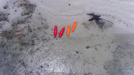 Orange and red kayaks on the beach shore.