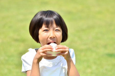 Girl eating a rice ball in grassの写真素材