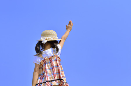 Girl raise hand in the blue sky (straw hat, back)