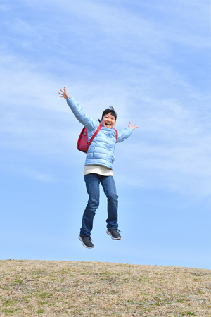 Japanese elementary school girl jumping  in the blue skyの写真素材
