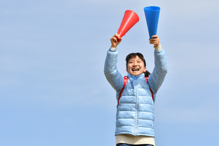 Japanese elementary school girl cheering with megaphone in the blue skyの写真素材