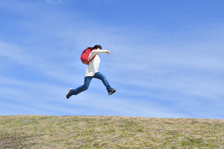 Japanese elementary school girl jumping in the blue skyの写真素材