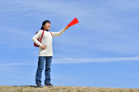 Japanese elementary school girl cheering with megaphone in the blue skyの写真素材