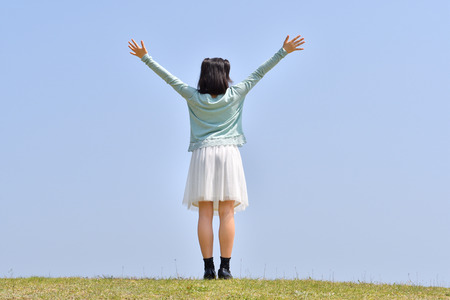 Japanese Girl raising hands in the blue Sky (Rear view)の写真素材
