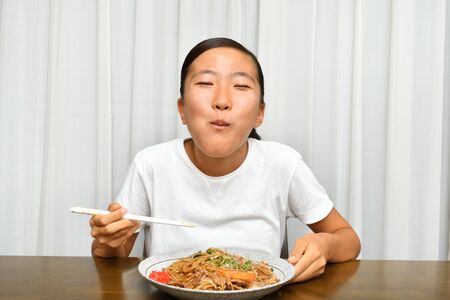 Japanese girl enjoys having stir fried noodles with vegetables and meatの写真素材