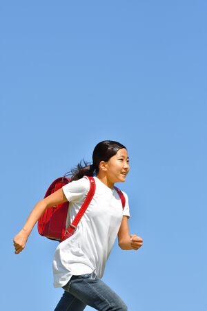 Japanese elementary school girl running in the blue skyの写真素材