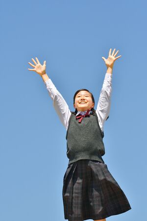 Japanese girl raising hands in the blue skyの写真素材
