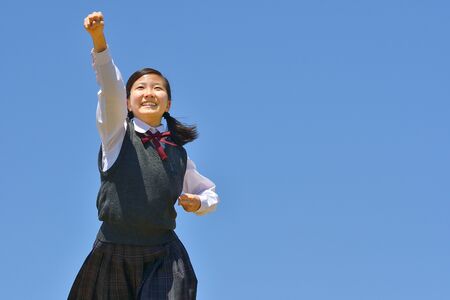 Japanese girl strikes a victory pose in the blue skyの写真素材