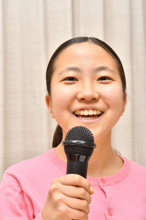 Japanese girl enjoys singing a song by the microphoneの写真素材