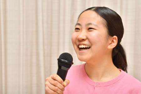 Japanese girl enjoys singing a song by the microphoneの写真素材