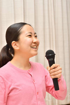 Japanese girl enjoys singing a song by the microphoneの写真素材