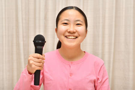 Japanese girl enjoys singing a song by the microphoneの写真素材